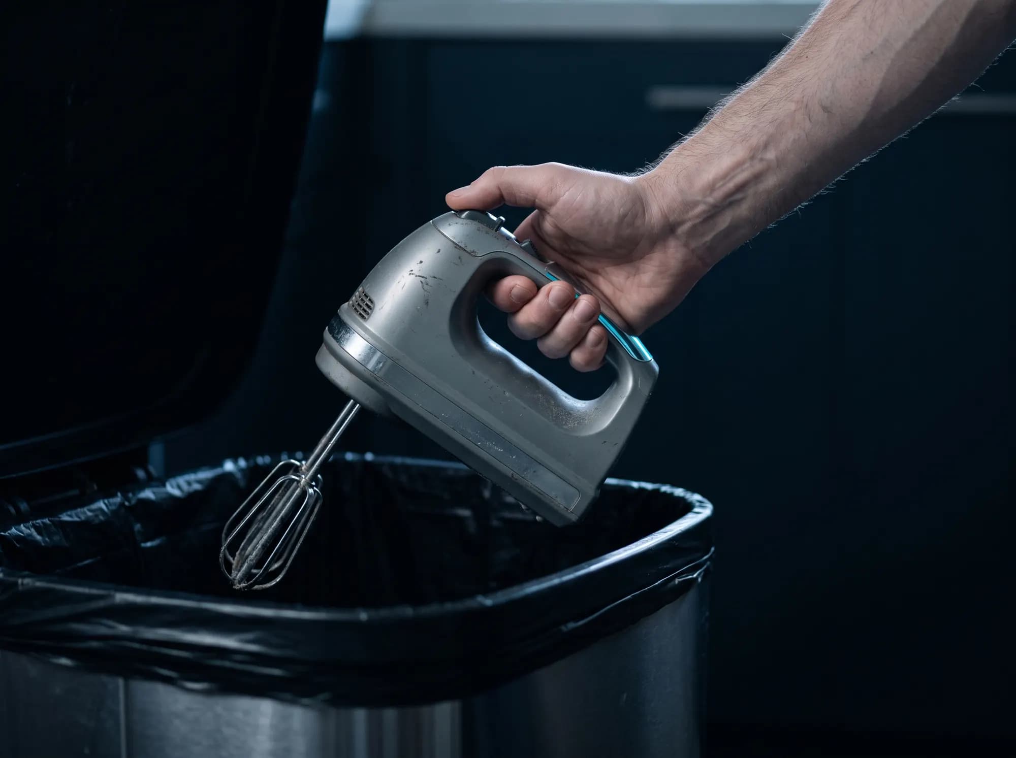 A hand holding a working but unloved food mixer over an open kitchen bin, paused.