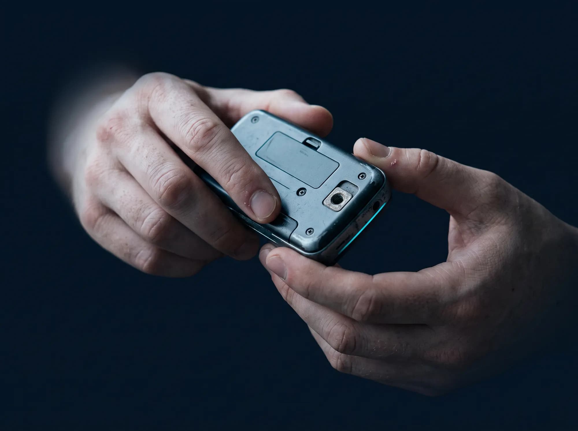 Two hands turning a small second-hand device over, examining its underside in cool window light.